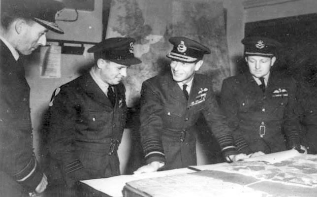 Air Vice-Marshal Ralph Cochrane, Wing Commander Guy Gibson, King George VI and Group Captain John Whitworth discussing the Operation Chastise 'Dambusters Raid'Hensser (F/O), Royal Air Force official photographer, Public domain, via Wikimedia Commons