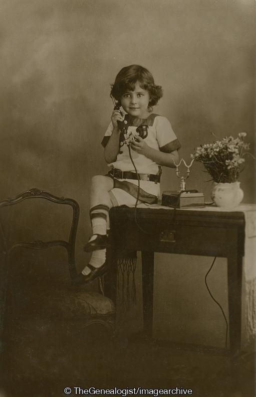 Child on desk with phone and plant (C1900, Child, desk, flowers, Telephone)